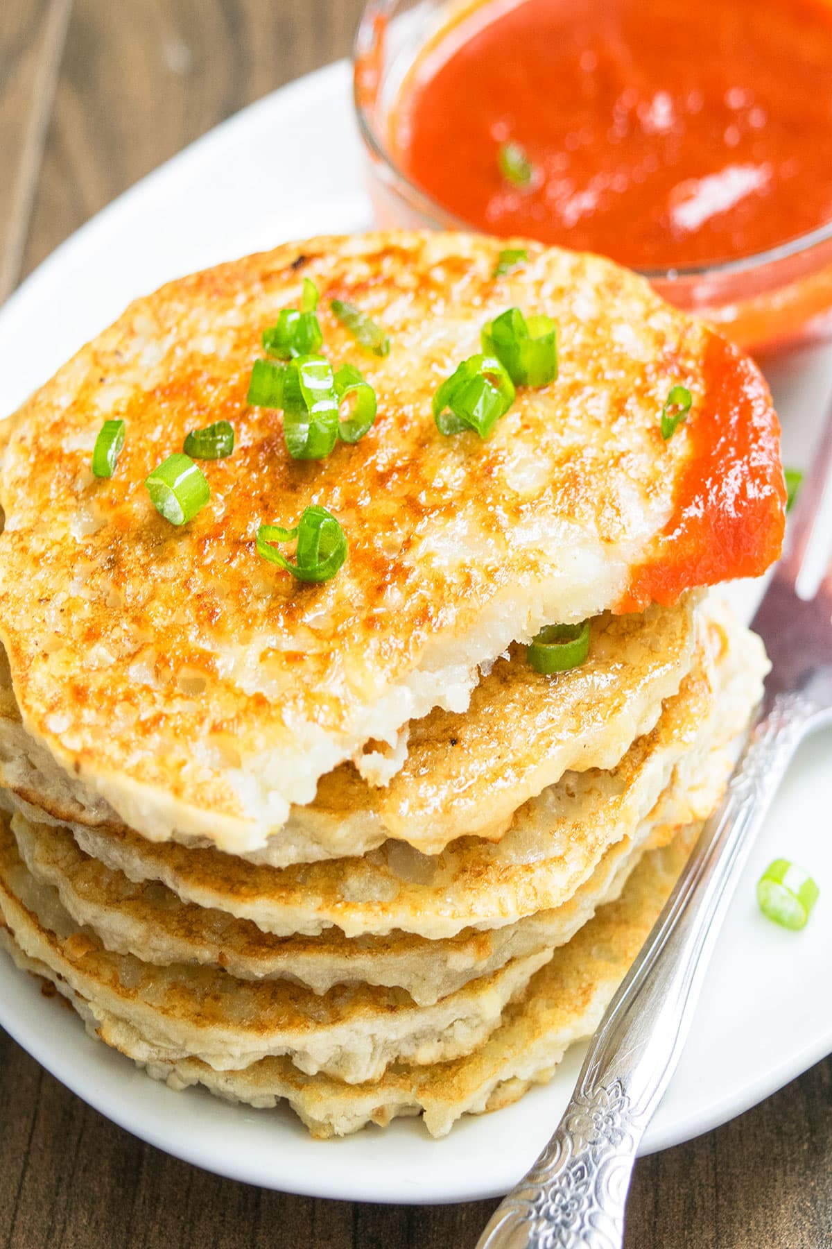 Partially eaten savory pancake dipped in sriracha sauce. 