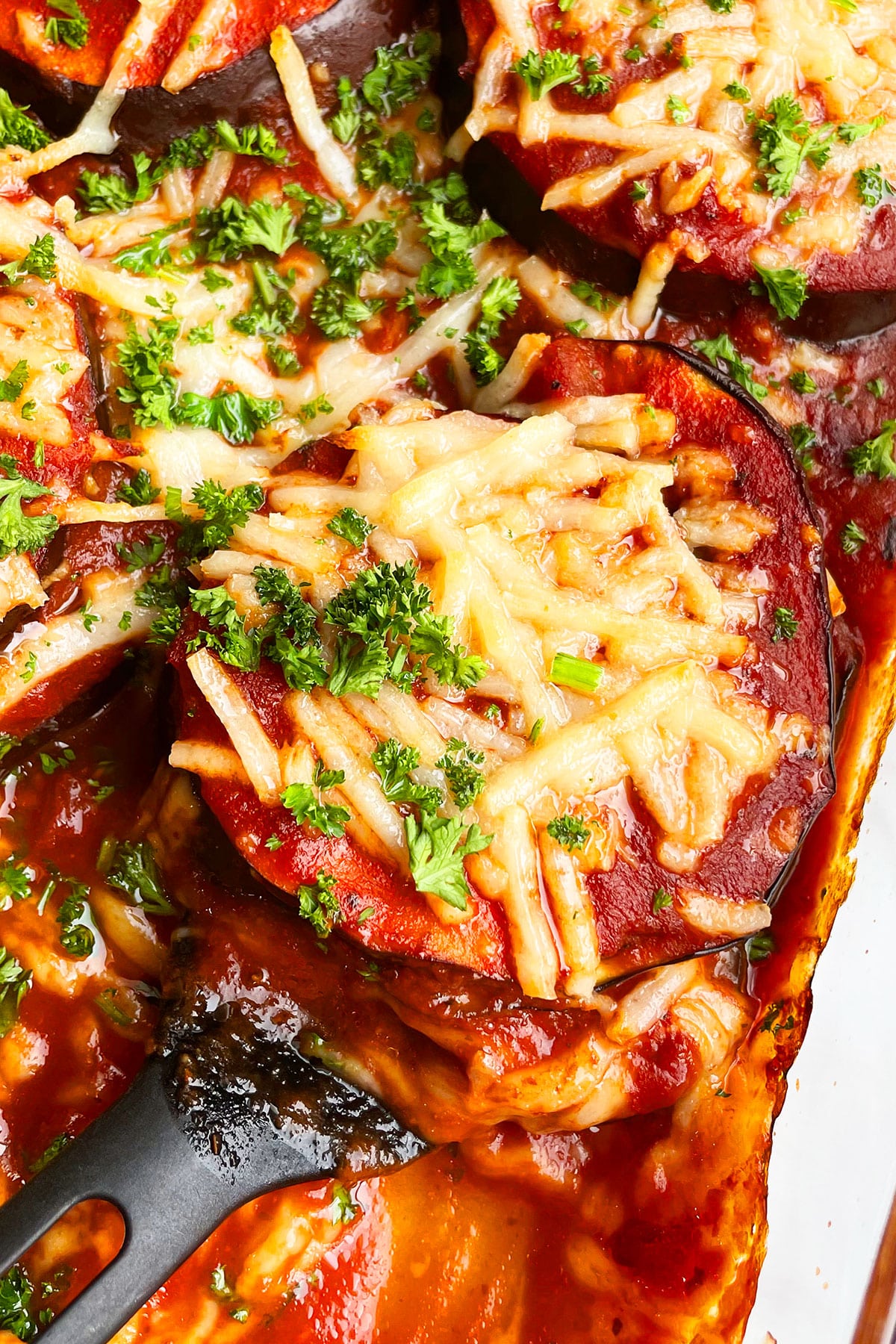 Closeup shot of cheesy aubergine lasagna with parsley garnish in glass baking dish. 