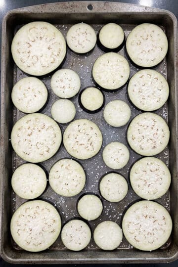 Round eggplant slices sweating with salt on baking tray. 