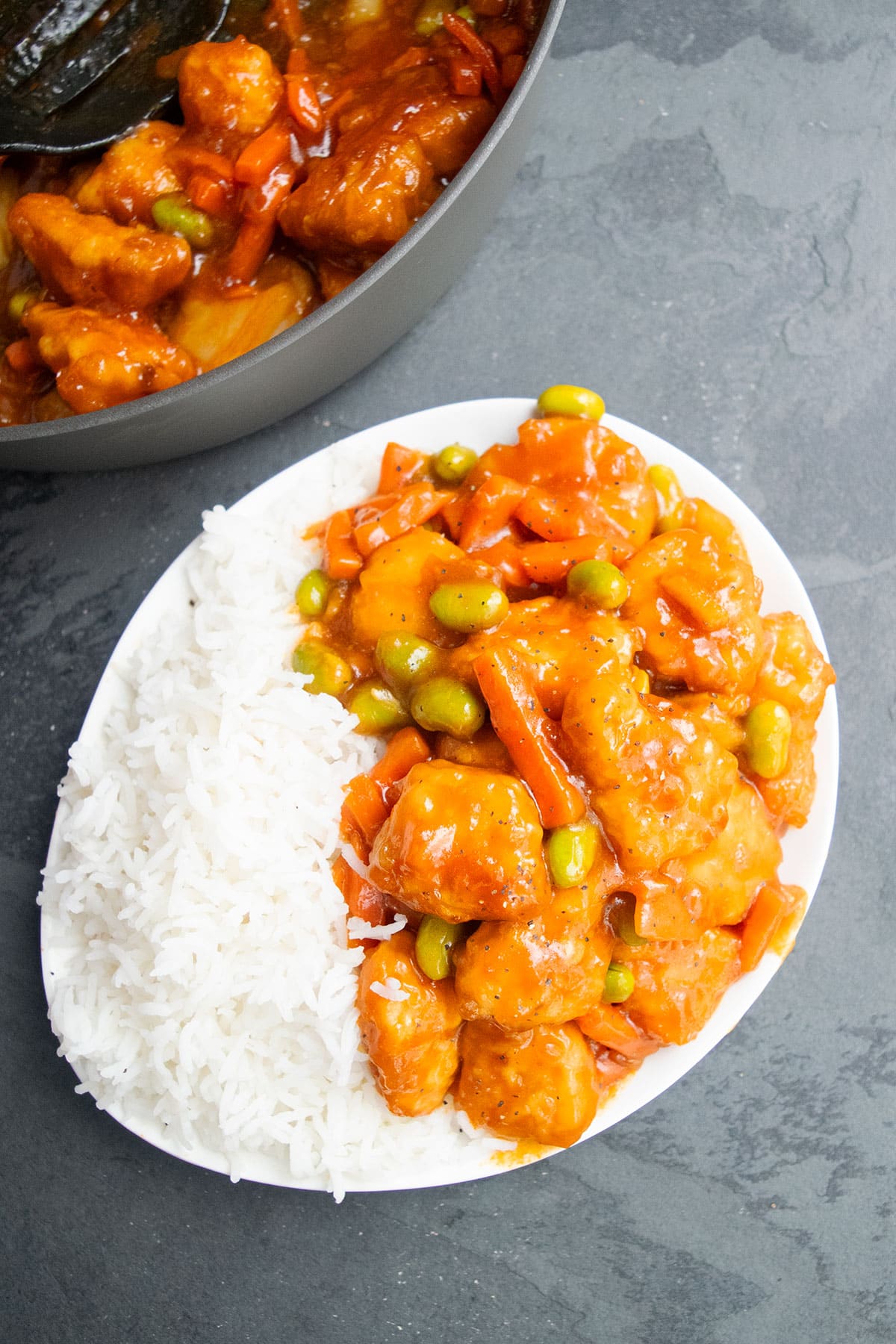 Asian chicken with veggies and sauce served in white dish with steamed rice. 