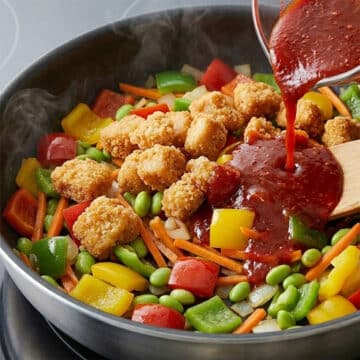 Breaded chicken and sauce being added on top of the veggies in nonstick pan. 