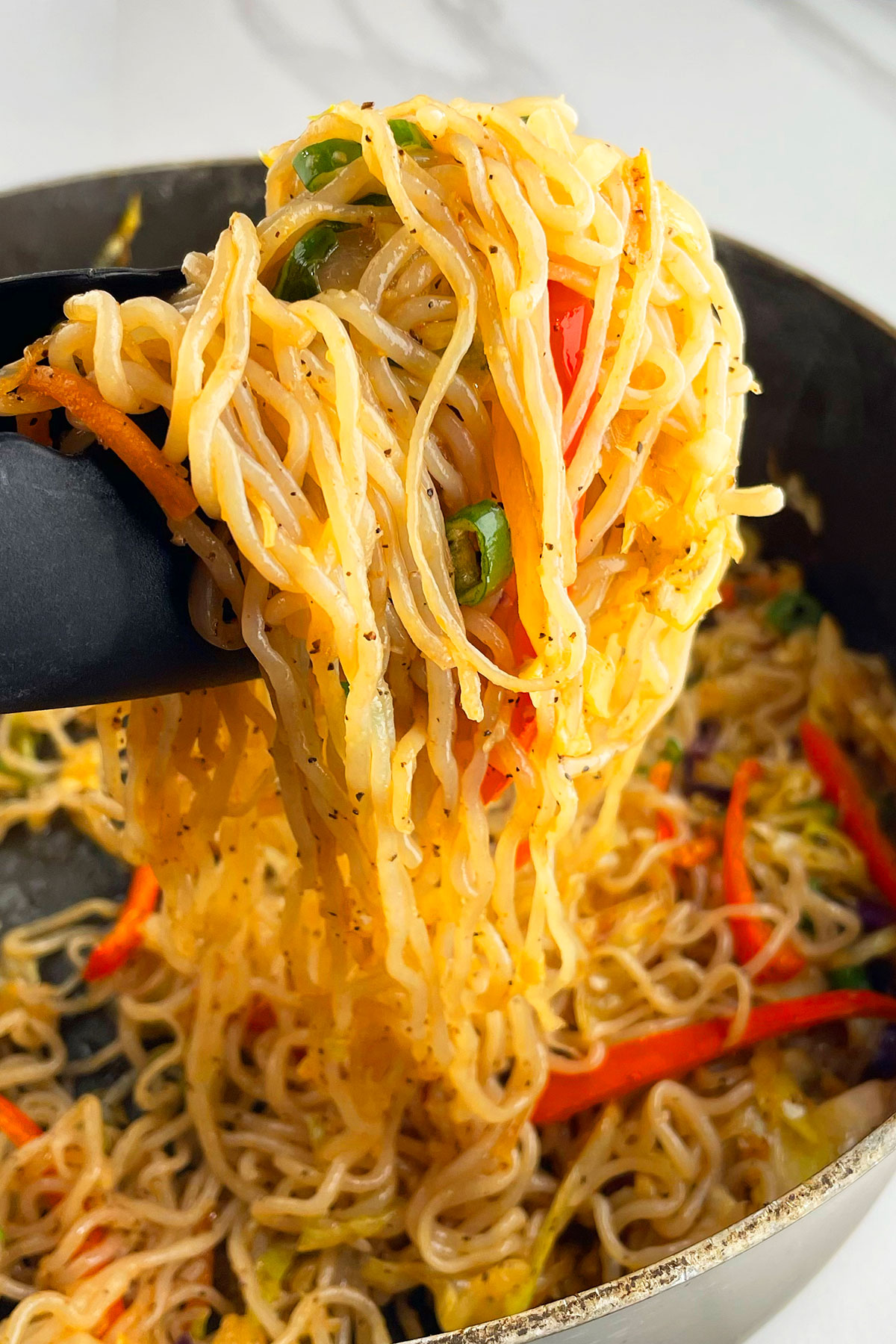 Closeup shot of stir fried noodles and veggies in a tong.