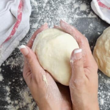 Hands being used to form dough into a ball shape. 