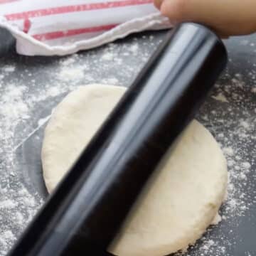 Dough being rolled out with a black rolling pin. 
