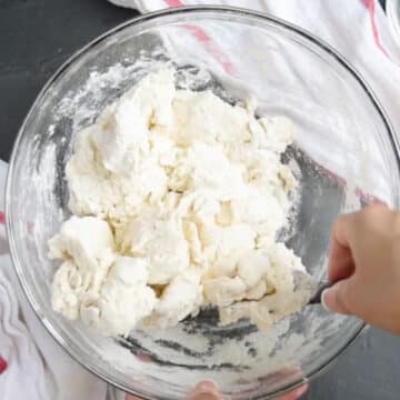 Yogurt and flour being mixed together with a spoon in glass bowl. 